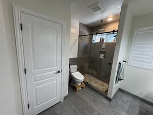 Bathroom featuring an enclosed shower, toilet, and a textured ceiling