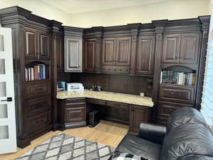 Office space with ornamental molding, built in desk, and light hardwood / wood-style floors