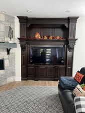 Living room featuring a stone fireplace, ornamental molding, a textured ceiling, and light wood-type flooring