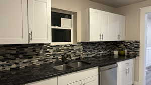 Kitchen with dark stone counters, dishwasher, sink, and white cabinets