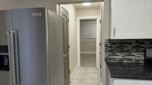 Kitchen with tasteful backsplash, high end refrigerator, white cabinets, ornamental molding, and light tile patterned floors