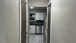 Kitchen featuring backsplash, dishwasher, light tile patterned flooring, and white cabinets