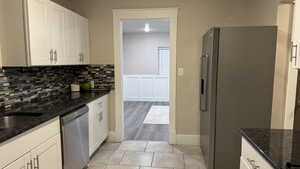 Kitchen featuring appliances with stainless steel finishes, dark stone countertops, backsplash, white cabinets, and light tile patterned flooring