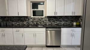 Kitchen featuring dark stone countertops, sink, stainless steel dishwasher, and white cabinets