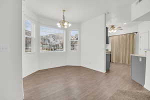 Unfurnished dining area featuring ceiling fan with notable chandelier and light hardwood / wood-style floors