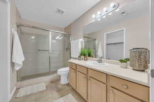 Bathroom featuring vanity, a textured ceiling, tile patterned floors, toilet, and walk in shower