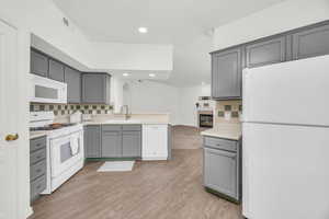 Kitchen featuring sink, gray cabinetry, light hardwood / wood-style flooring, white appliances, and decorative backsplash