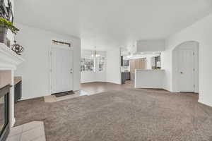 Unfurnished living room with ceiling fan with notable chandelier, a tile fireplace, and light carpet