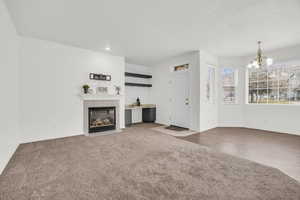 Unfurnished living room with light carpet, a fireplace, a textured ceiling, and an inviting chandelier