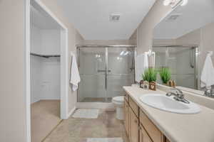 Bathroom featuring vanity, a shower with shower door, toilet, and a textured ceiling