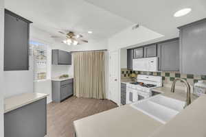 Kitchen featuring tasteful backsplash, sink, gray cabinetry, white appliances, and light hardwood / wood-style flooring