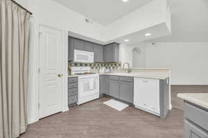 Kitchen with sink, white appliances, light hardwood / wood-style flooring, gray cabinetry, and backsplash