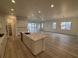 Kitchen featuring pendant lighting, dishwasher, sink, white cabinets, and a kitchen island with sink