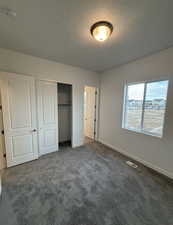 Unfurnished bedroom featuring a textured ceiling, dark carpet, and a closet