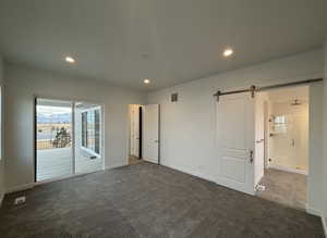 Unfurnished bedroom with ensuite bathroom, access to outside, a barn door, and dark colored carpet