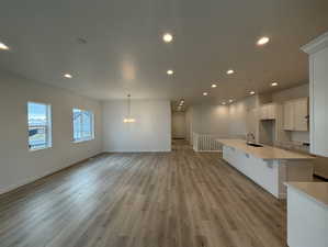 Unfurnished living room featuring an inviting chandelier, sink, and light hardwood / wood-style flooring