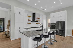 Kitchen featuring sink, an island with sink, wall chimney exhaust hood, and appliances with stainless steel finishes