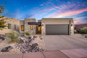 View of front of property featuring a garage, concrete driveway, stone siding, and stucco siding