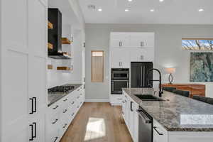 Kitchen with sink, appliances with stainless steel finishes, a kitchen island with sink, white cabinets, and wall chimney exhaust hood