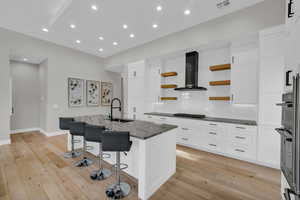 Kitchen with sink, a kitchen breakfast bar, an island with sink, dark stone counters, and wall chimney exhaust hood