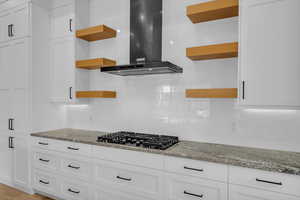 Kitchen with white cabinetry, light stone countertops, wall chimney range hood, and black gas stovetop