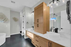 Full bath with double vanity, tile patterned floors, baseboards, a freestanding bath, and a shower with shower door