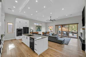 Kitchen with a sink, black appliances, light wood-style flooring, light stone counters, and open floor plan