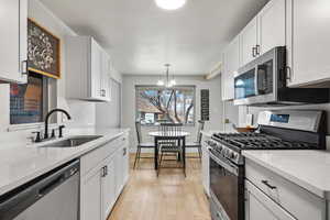 Kitchen with sink, white cabinetry, light hardwood / wood-style flooring, pendant lighting, and stainless steel appliances