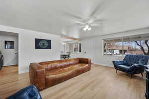 Living room featuring ceiling fan with notable chandelier and light wood-type flooring