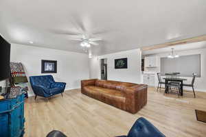 Living room featuring ceiling fan with notable chandelier and light hardwood / wood-style flooring