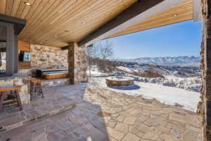 Snow covered patio with a mountain view, a hot tub, and an outdoor fire pit