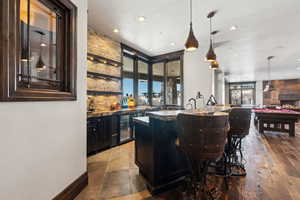 Bar featuring hanging light fixtures, beverage cooler, and dark stone counters