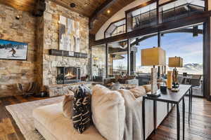 Living room featuring wood-type flooring, a stone fireplace, beam ceiling, and wooden ceiling