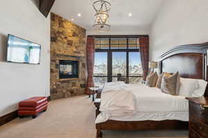 Carpeted bedroom featuring an inviting chandelier, a towering ceiling, a mountain view, a stone fireplace, and access to outside