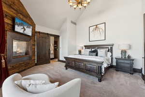 Bedroom featuring an inviting chandelier, a barn door, high vaulted ceiling, and light carpet