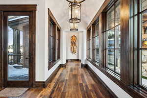 Corridor featuring dark hardwood / wood-style flooring, lofted ceiling, a wealth of natural light, and a chandelier