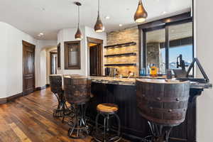 Bar with hanging light fixtures and dark hardwood / wood-style flooring