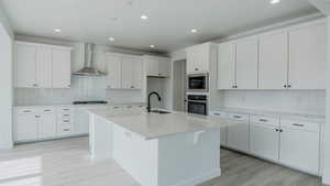 Kitchen with light countertops, appliances with stainless steel finishes, white cabinets, a sink, and wall chimney range hood