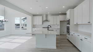 Kitchen with white cabinets, wall chimney exhaust hood, light countertops, and oven