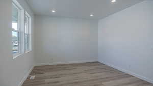 Empty room featuring light wood-style floors, recessed lighting, visible vents, and baseboards