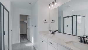 Full bath featuring double vanity, a stall shower, a spacious closet, and a sink