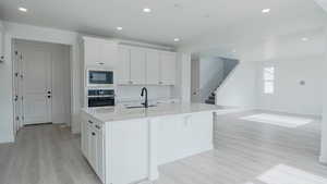 Kitchen featuring a kitchen island with sink, white cabinets, a sink, built in microwave, and oven