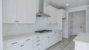 Kitchen with light countertops, stainless steel gas stovetop, light wood-style floors, white cabinetry, and wall chimney exhaust hood