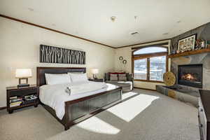 Bedroom with light carpet, crown molding, and a fireplace