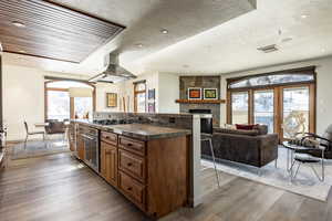 Kitchen featuring a breakfast bar area, appliances with stainless steel finishes, island range hood, a fireplace, and light hardwood / wood-style floors