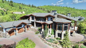 View of front facade with stone siding, a wooded view, a balcony, and driveway