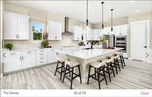 Kitchen with white cabinetry, wall chimney range hood, a kitchen island with sink, and appliances with stainless steel finishes