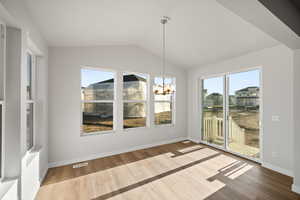 Unfurnished dining area with wood-type flooring, vaulted ceiling, and a notable chandelier