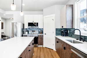 Kitchen with appliances with stainless steel finishes, decorative light fixtures, sink, white cabinets, and light wood-type flooring