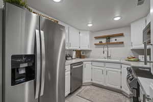 Kitchen with sink, light tile patterned floors, white cabinetry, stainless steel appliances, and light stone countertops